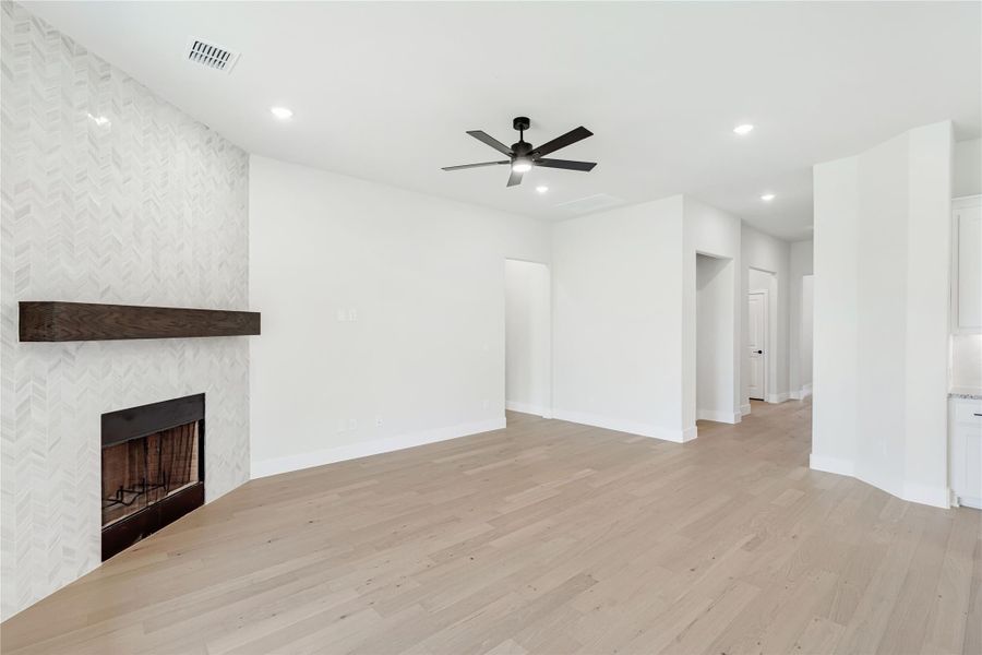 Open living room with herringbone tile fireplace, wood mantel, ceiling fan, and light hardwood floors