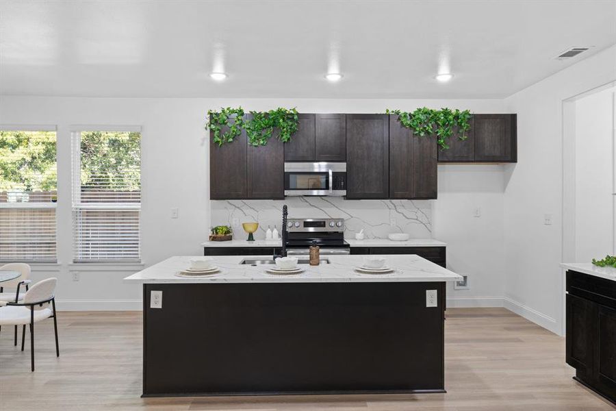 Kitchen with tasteful backsplash, light stone counters, appliances with stainless steel finishes, light hardwood / wood-style floors, and a center island