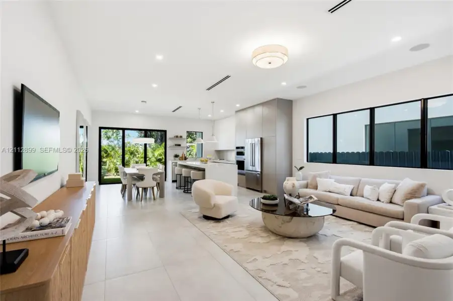 Open-concept interior featuring large-format tile flooring, recessed ceiling lighting, built-in kitchen cabinetry, stainless steel appliances, and black-framed windows