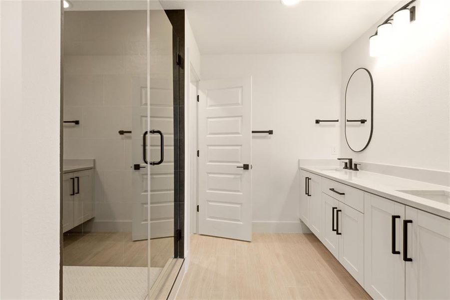 Full bath with double vanity, a stall shower, and light wood-style floors