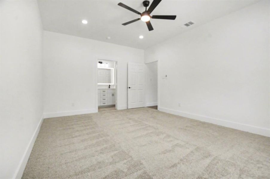 Spacious room featuring light-colored carpeting, a ceiling fan with integrated lighting, recessed lighting, and a white door, with a glimpse of a bathroom vanity and mirror through an open doorway