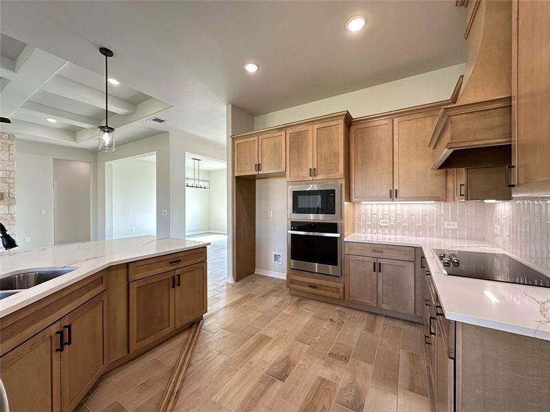 Kitchen featuring stainless steel oven, light stone counters, brown cabinetry, coffered ceiling, and wood finish floors