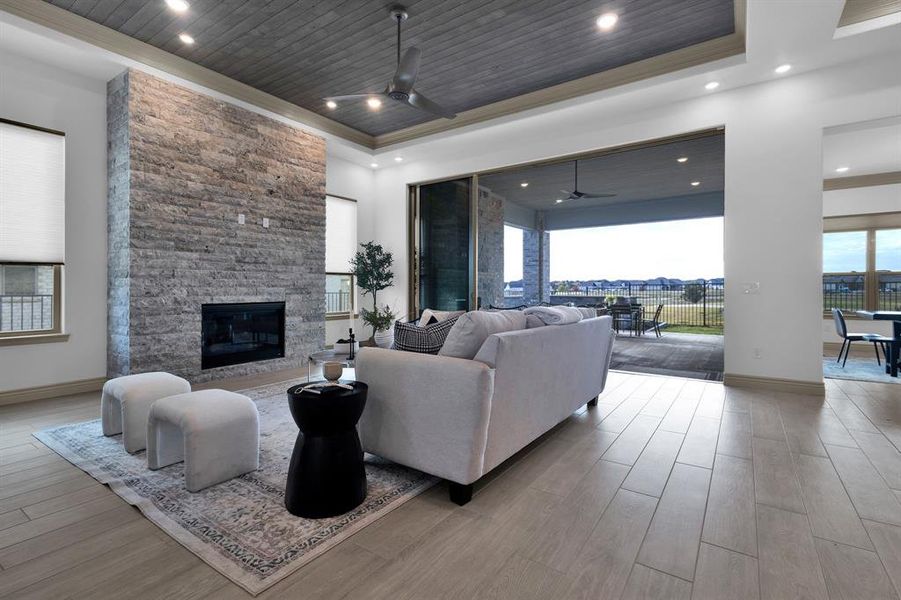 Living room featuring wooden ceiling, light wood-style flooring, ceiling fan, a stone fireplace, and a tray ceiling