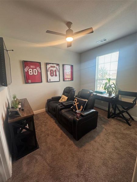 Living area with dark carpet, a textured ceiling, and a ceiling fan Living area with dark carpet, a textured ceiling, and a ceiling fan
