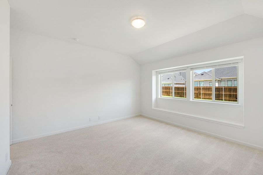 Empty bedroom with vaulted ceiling, carpet flooring, and large triple-pane window overlooking backyard fence Empty bedroom with vaulted ceiling, carpet flooring, and large triple-pane window overlooking backyard fence