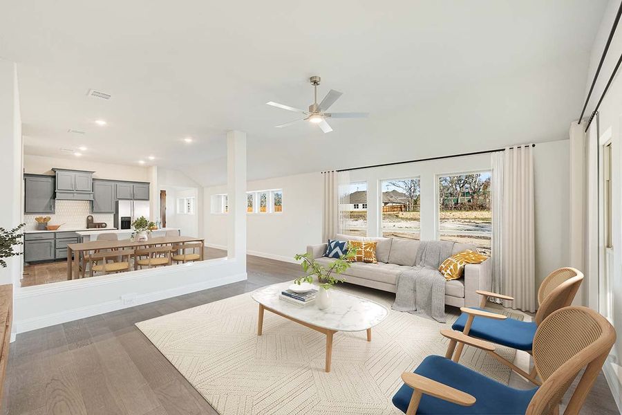 Open-concept living room with ceiling fan, hardwood floors, and view into kitchen and dining area