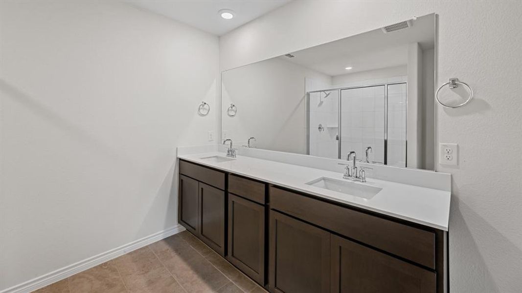 Bathroom featuring a dual-sink vanity with dark wood-finish cabinetry and light-toned countertops Bathroom featuring a dual-sink vanity with dark wood-finish cabinetry and light-toned countertops
