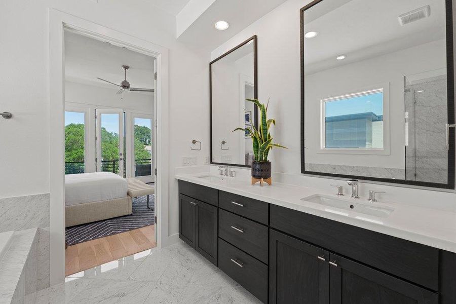 Luxurious primary bathroom showcasing a dual-sink vanity with dark cabinetry, sleek white countertops, and upscale finishes.