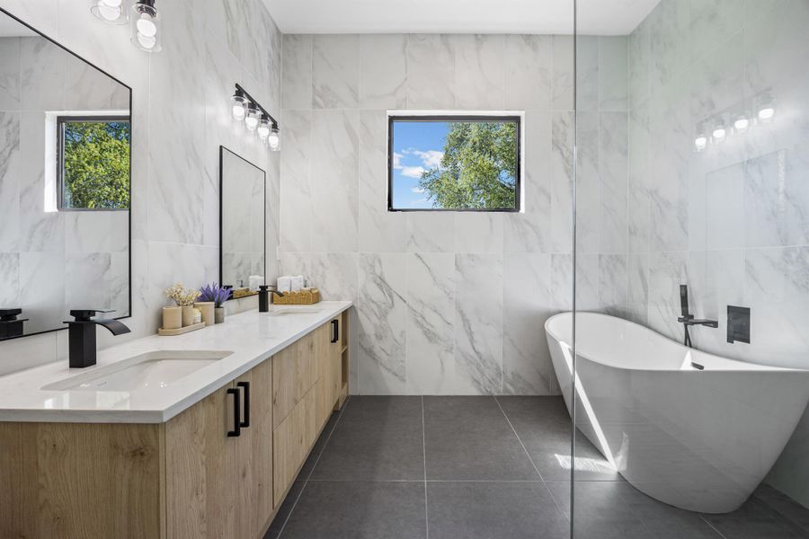 Bathroom featuring double vanity, tile walls, a soaking tub, and dark tile patterned flooring