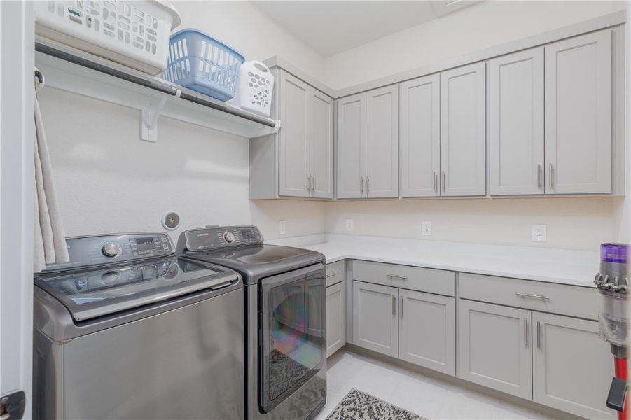 Spacious and well-equipped laundry room with overhead hanging rails, multiple cabinets, clean tile floors and wall mounted outlets for utility equipment.