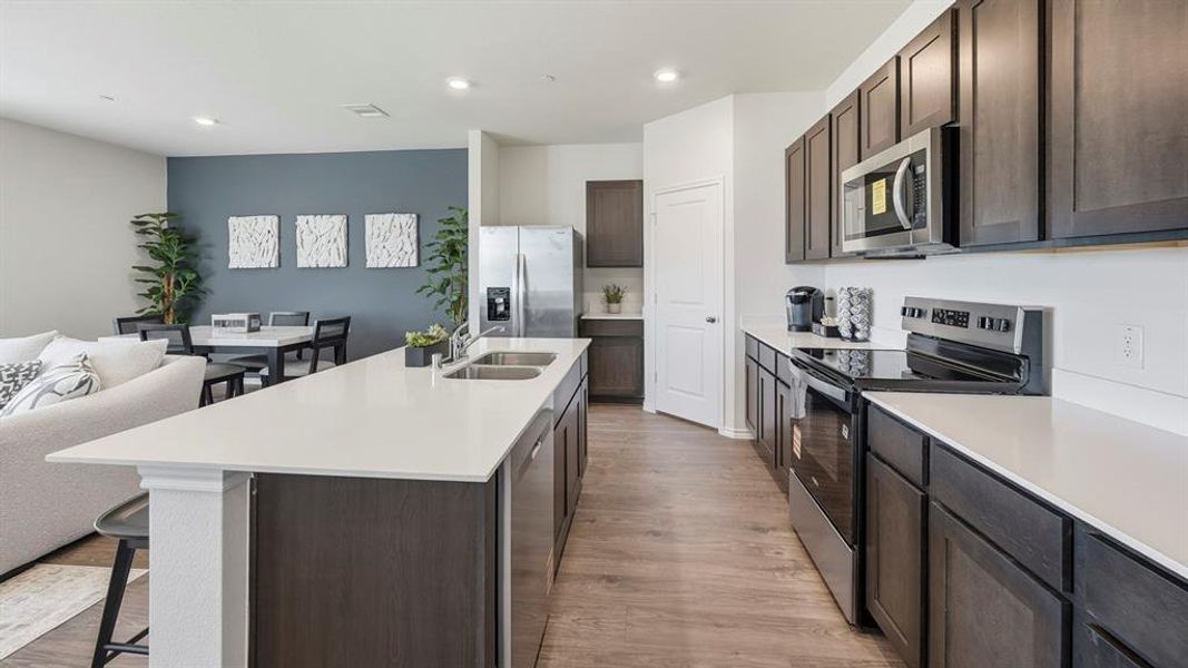 Kitchen featuring dark brown cabinetry, stainless steel appliances, light wood finished floors, a kitchen island with sink, and a kitchen bar Kitchen featuring dark brown cabinetry, stainless steel appliances, light wood finished floors, a kitchen island with sink, and a kitchen bar