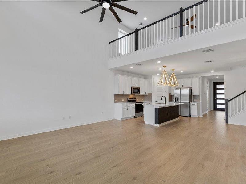 Unfurnished living room with a ceiling fan, light wood finished floors, recessed lighting, a high ceiling, and stairs