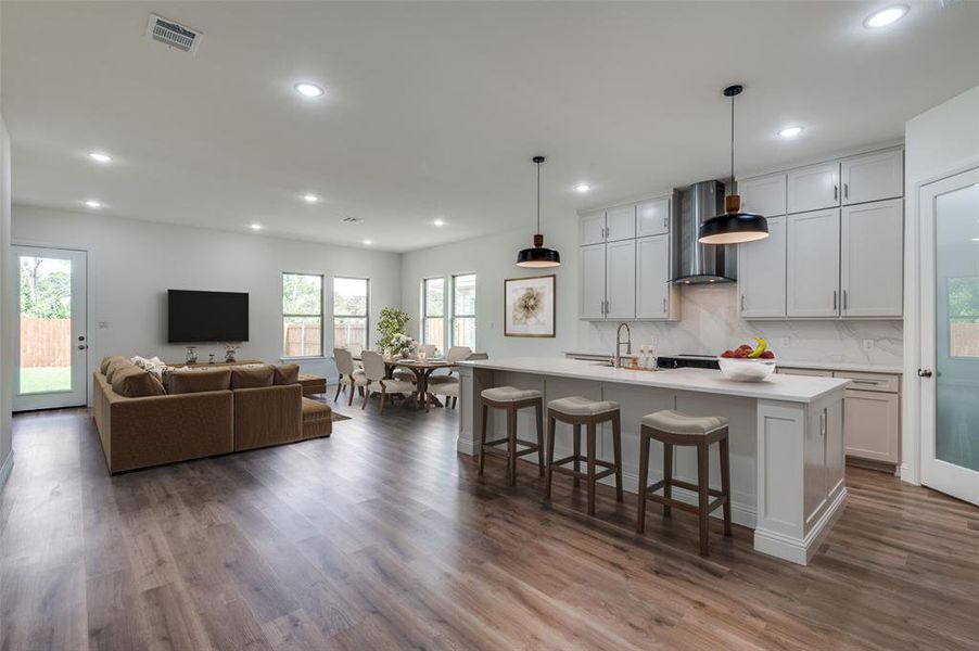 Virtually Staged for Illustrative Purposes.
Kitchen featuring a kitchen island with sink, dark hardwood / wood-style floors, a breakfast bar, wall chimney exhaust hood, and pendant lighting