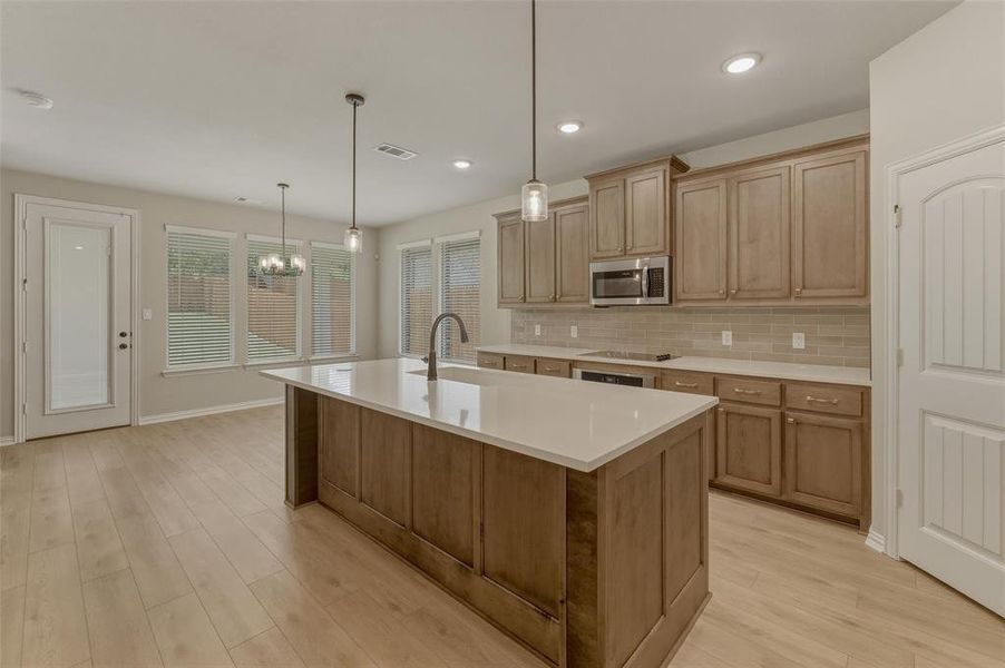 Open-concept kitchen featuring an oversized island with white countertop, wood-finish flooring, and pendant lighting
