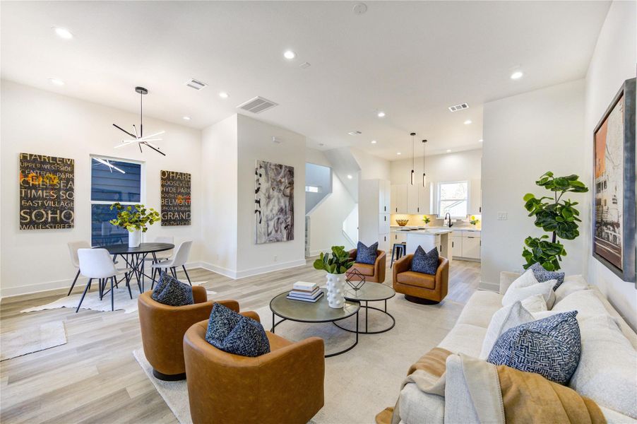 This is a modern, open-concept living space featuring a cozy seating area with stylish chairs and a sofa, a dining nook with contemporary lighting, and a sleek kitchen with an island. The room is bright and inviting, with tasteful decor and natural light.