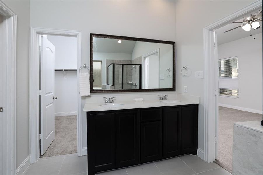 Bathroom with double vanity, ceiling fan, tile patterned flooring, a shower stall, and a walk in closet