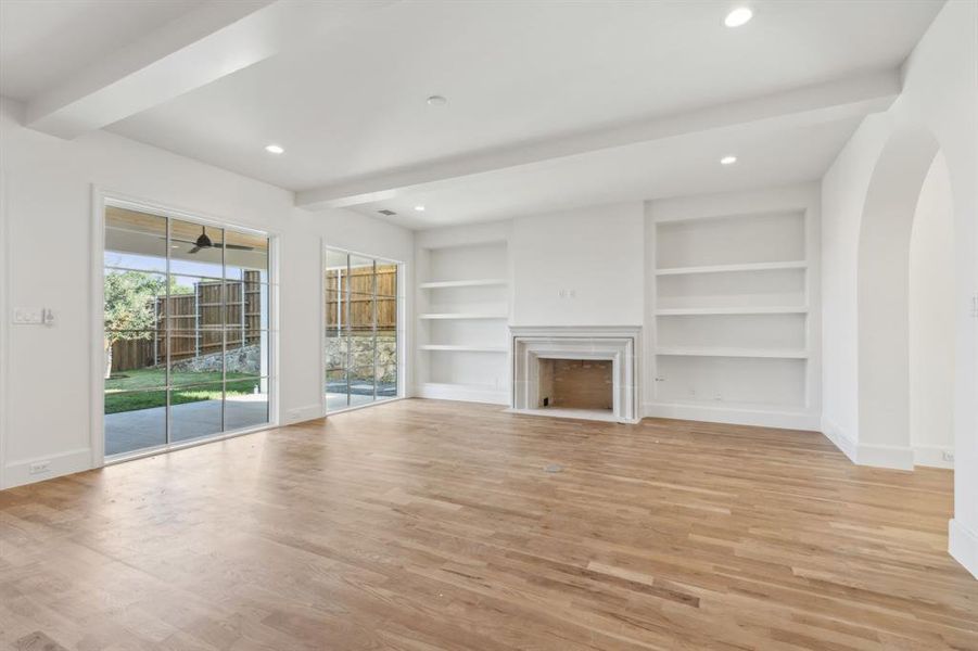 Living room with beamed ceiling, built in shelves, and light hardwood flooring