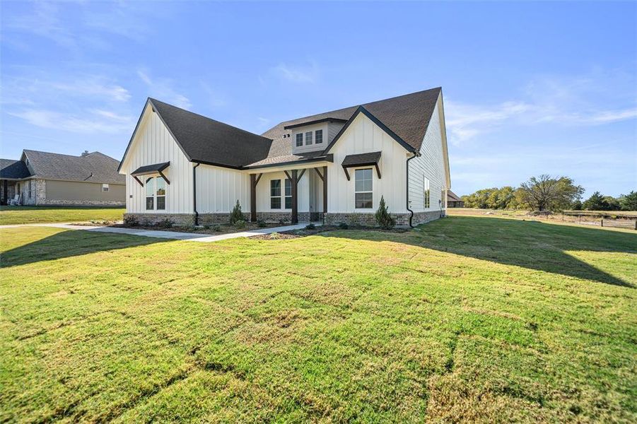 Modern farmhouse with board and batten siding, a front yard, covered porch, and a shingled roof