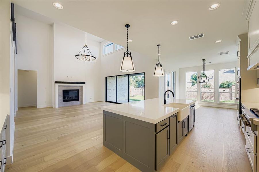 Kitchen featuring hanging light fixtures, recessed lighting, a tiled fireplace, a kitchen island with sink, and open floor plan Kitchen featuring hanging light fixtures, recessed lighting, a tiled fireplace, a kitchen island with sink, and open floor plan