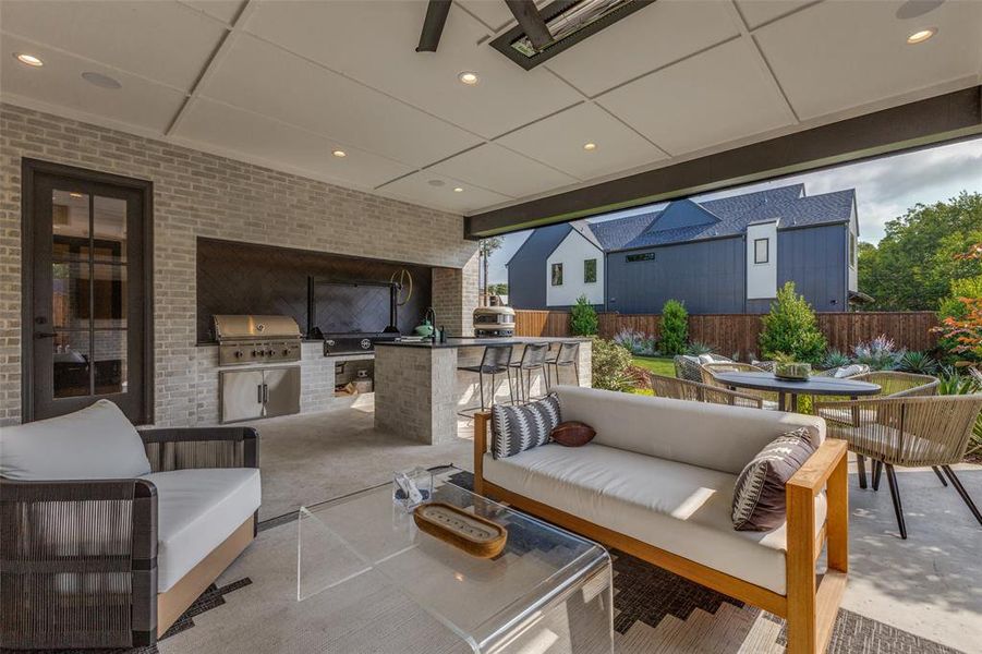 Covered outdoor patio featuring a built-in grill, stone island with bar seating, recessed lighting, and a brick accent wall Covered outdoor patio featuring a built-in grill, stone island with bar seating, recessed lighting, and a brick accent wall
