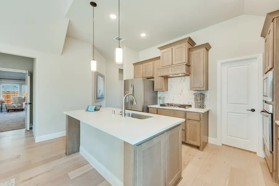 Kitchen with center island, sink, tan cabinets, tile backsplash, and pendant lights over light wood floors