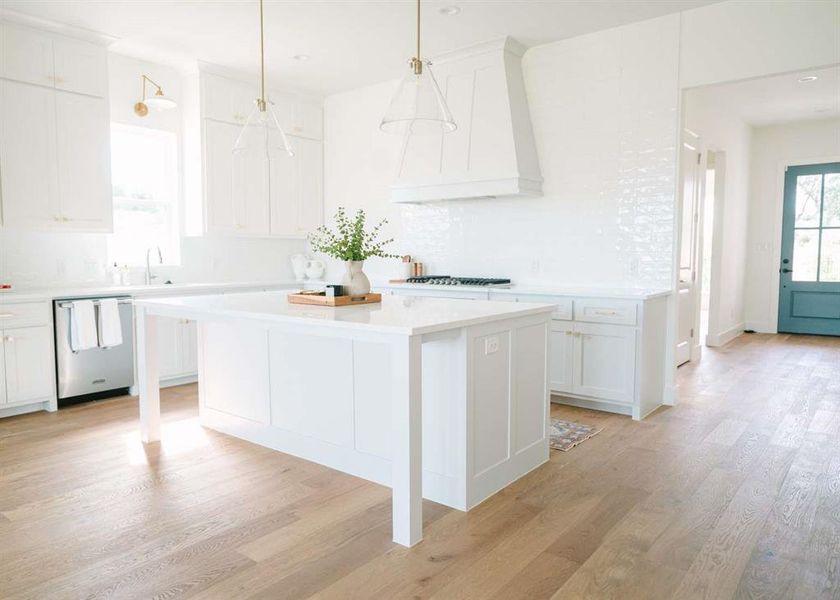 Kitchen featuring light hardwood / wood-style flooring, a kitchen island, stainless steel appliances, white cabinets, and premium range hood