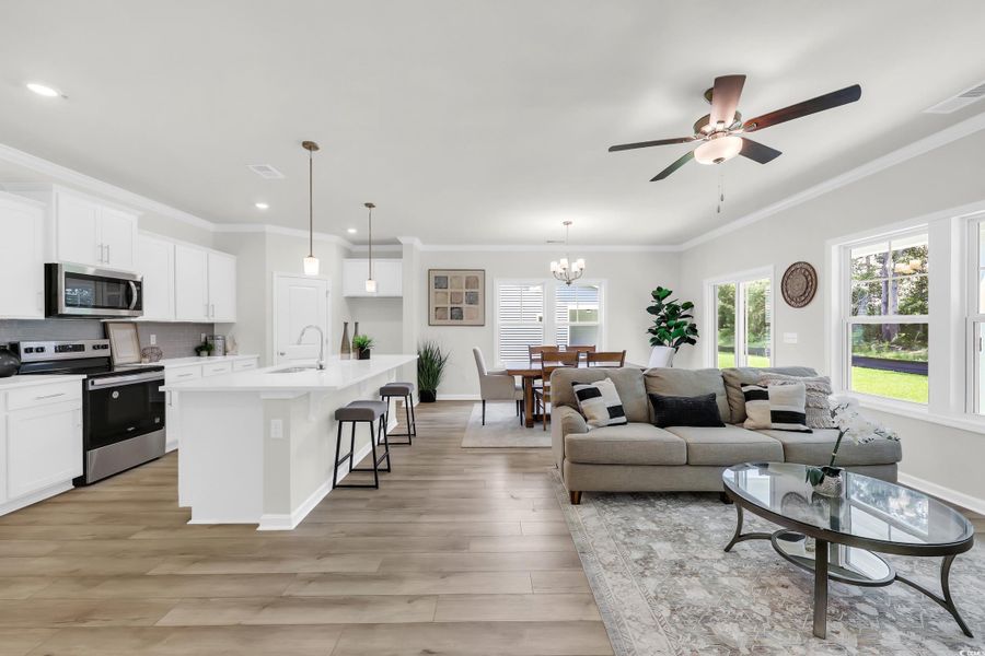Living room with a chandelier, crown molding, a ceiling fan, and light wood finished floors Living room with a chandelier, crown molding, a ceiling fan, and light wood finished floors