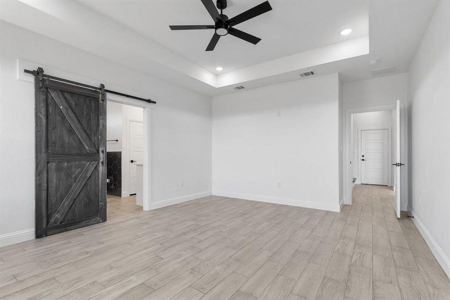 Unfurnished room with ceiling fan, a barn door, a raised ceiling, and light hardwood / wood-style flooring