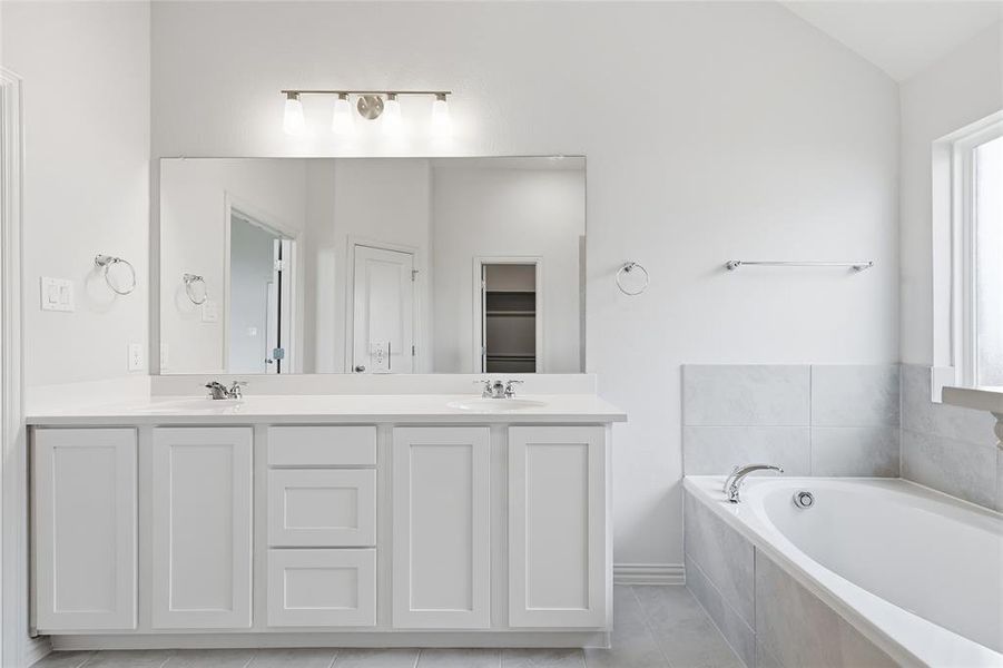 Bathroom featuring a bath, double vanity, lofted ceiling, and light tile patterned floors Bathroom featuring a bath, double vanity, lofted ceiling, and light tile patterned floors