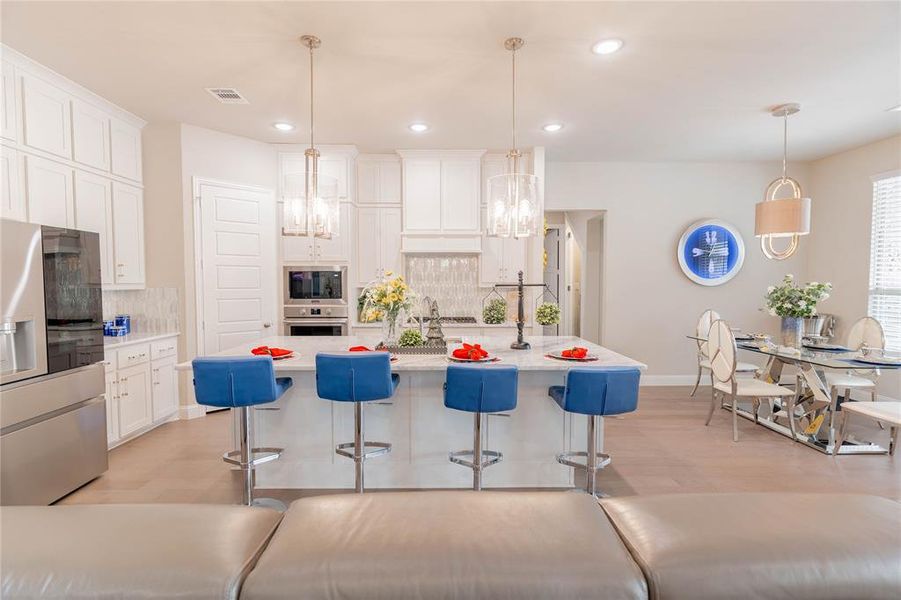 Kitchen featuring stainless steel appliances, a kitchen bar, tasteful backsplash, white cabinets, and hanging light fixtures