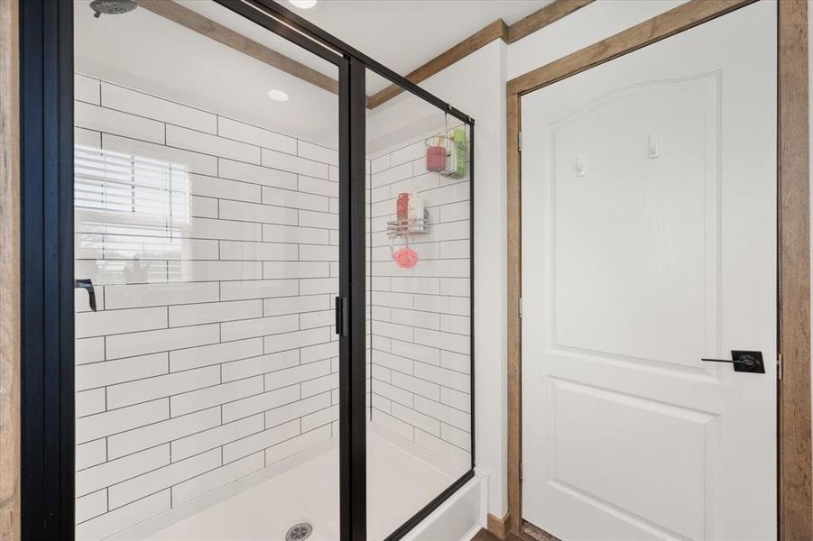 Walk-in shower featuring subway tile surround, matte black framed glass enclosure, and a rain showerhead