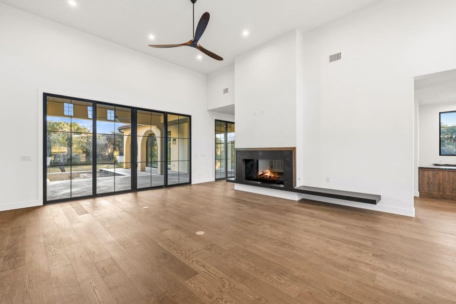 Unfurnished living room featuring a multi sided fireplace, a high ceiling, light wood-style floors, a ceiling fan, and recessed lighting