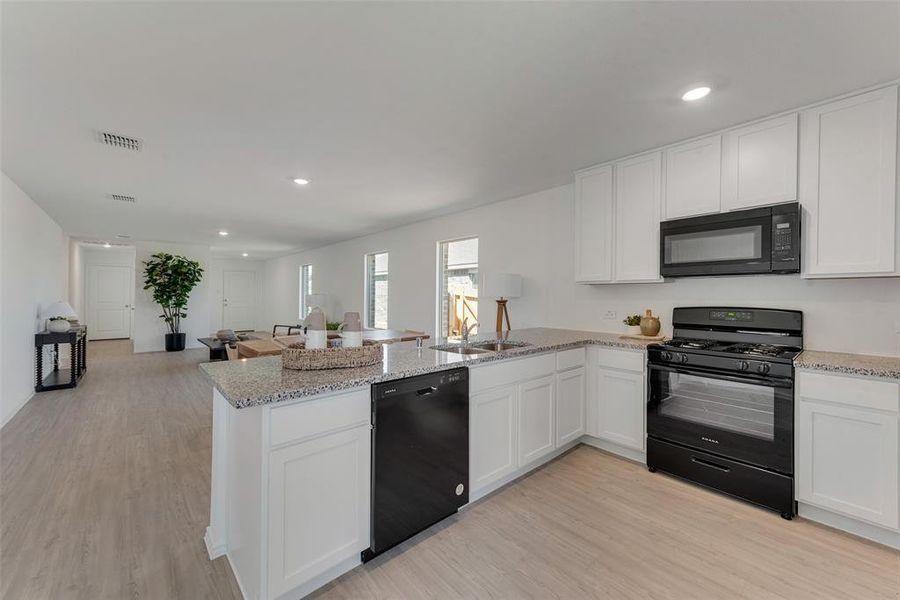 Kitchen with kitchen peninsula, white cabinetry, black appliances, and light hardwood / wood-style floors