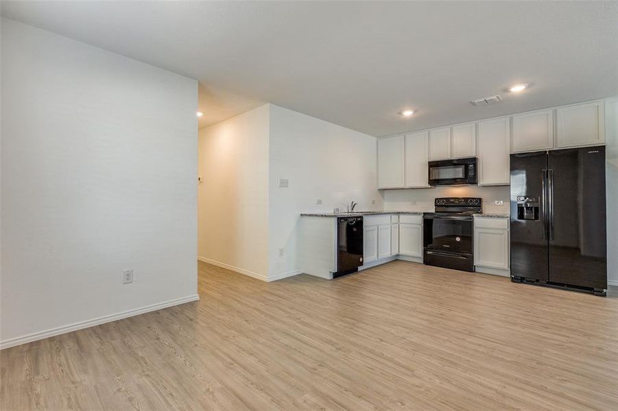 Kitchen with white cabinets, black appliances, and light wood-type flooring