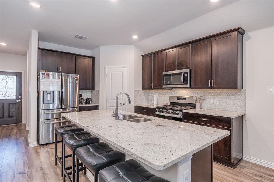 Kitchen with light stone counters, visible vents, appliances with stainless steel finishes, a sink, and an island with sink