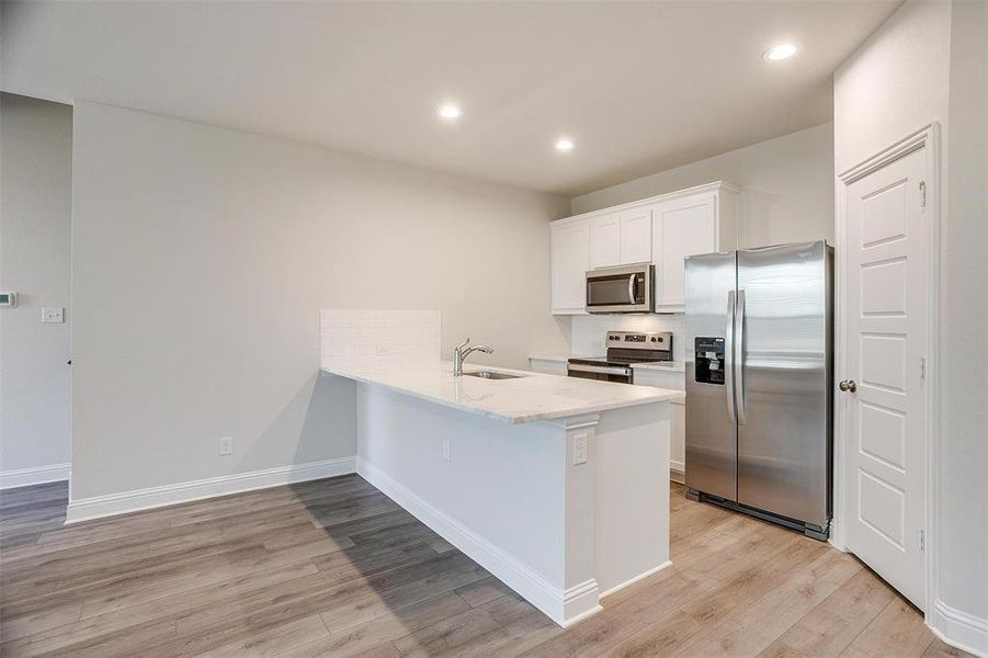 Kitchen with tasteful backsplash, appliances with stainless steel finishes, a sink, light wood-type flooring, and a peninsula