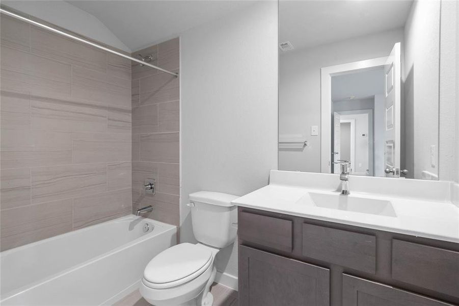 Secondary bath features tile flooring, tub/shower combo with tile surround, stained wood cabinets, beautiful light countertops, mirror, sleek fixtures and modern finishes.