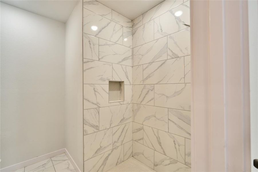 Shower enclosure featuring white marble-look subway tile walls, a built-in shower niche, and a white penny tile floor