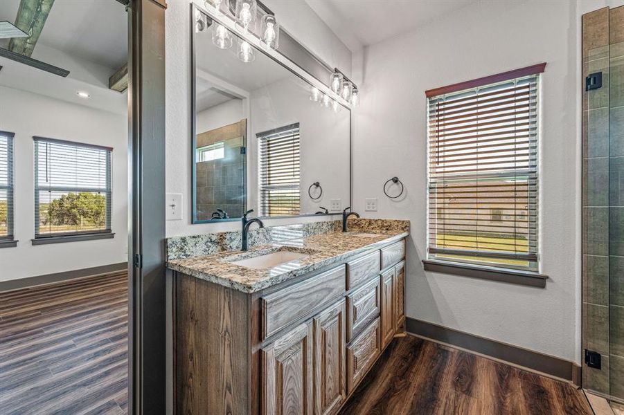 Full bathroom featuring double vanity, dark wood-type flooring, and tiled shower