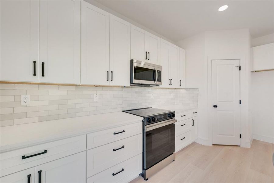 Kitchen featuring decorative backsplash, white cabinetry, appliances with stainless steel finishes, and light hardwood / wood-style flooring