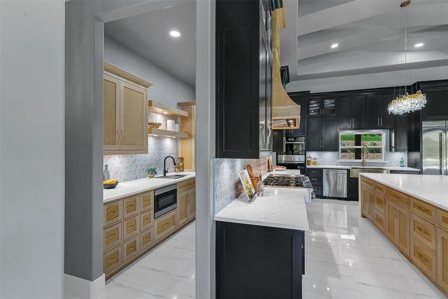 Kitchen with built in appliances, decorative light fixtures, tasteful backsplash, sink, and light brown cabinets