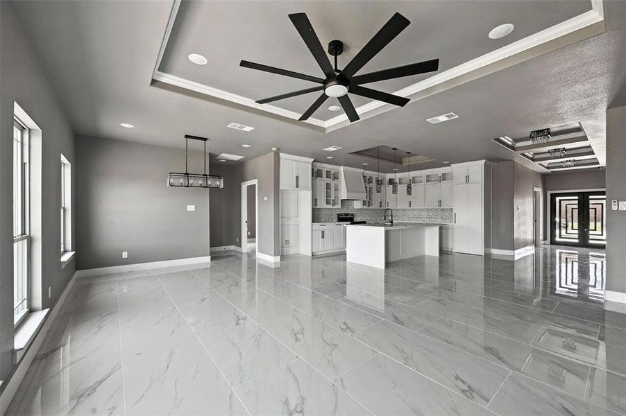 Unfurnished living room with a tray ceiling, ceiling fan, recessed lighting, ornamental molding, and light marble finish flooring Unfurnished living room with a tray ceiling, ceiling fan, recessed lighting, ornamental molding, and light marble finish flooring