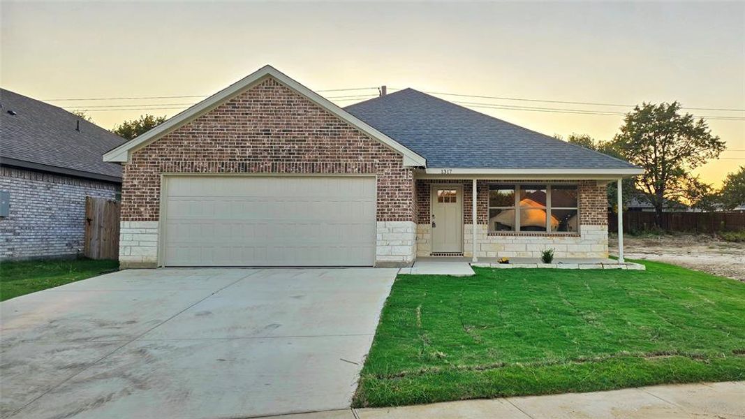 View of front of property featuring brick siding, a shingled roof, driveway, stone siding, and a garage