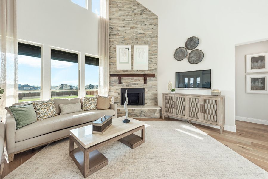 Living room with vaulted ceiling, floor-to-ceiling stone fireplace, hardwood floors, and large windows