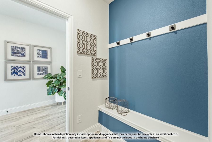 Mudroom entryway with blue accent wall, coat hooks, built-in bench, and view into adjacent room with framed wall art.