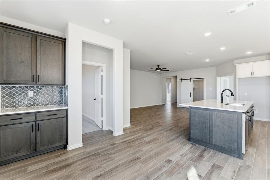 Kitchen with a barn door, a ceiling fan, decorative backsplash, a kitchen island with sink, and recessed lighting