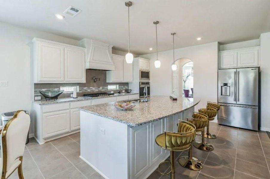 Kitchen with light stone counters, appliances with stainless steel finishes, and white cabinetry