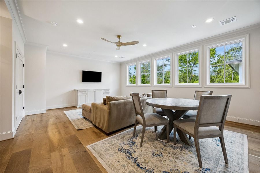 Spacious and light-filled game room featuring wide-plank French white oak flooring, crown molding & beautiful trim throughout. A wall of divided light windows brings in abundant natural light and overlooks the treetops, creating an inviting and functional atmosphere. Thoughtfully designed area which can be used for lounging and playing games.