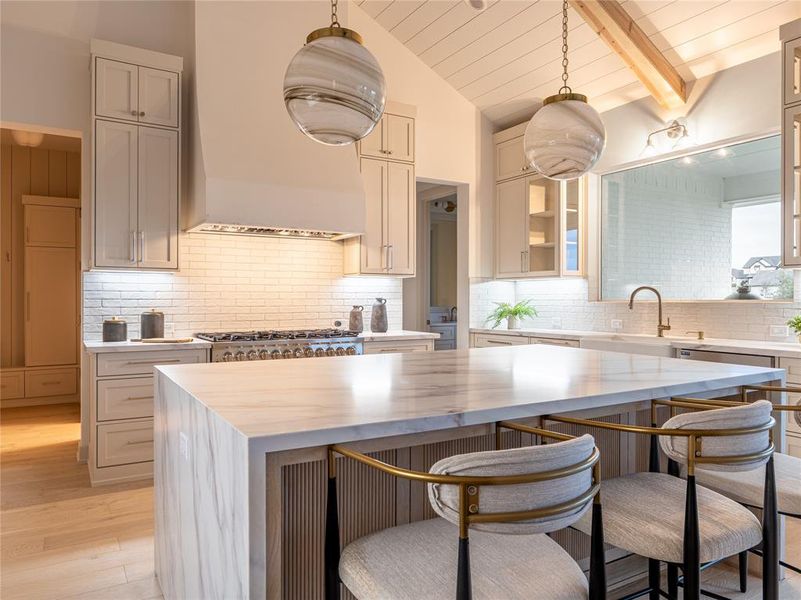 Kitchen featuring decorative backsplash, hanging light fixtures, custom exhaust hood, a center island, and light stone counters