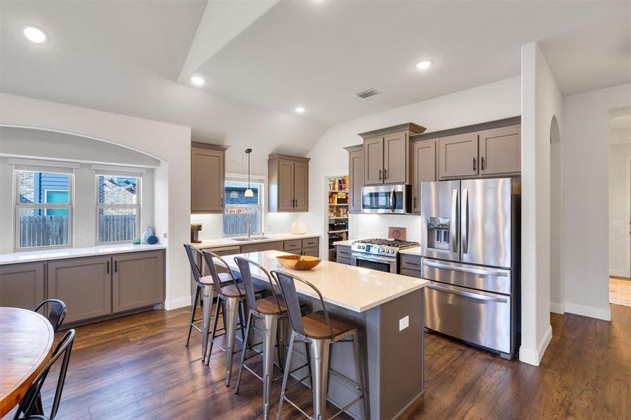 Kitchen with decorative light fixtures, dark wood-type flooring, appliances with stainless steel finishes, and vaulted ceiling